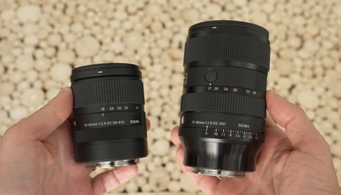 Two camera lenses held side-by-side for comparison, with the right lens noticeably larger than the left.