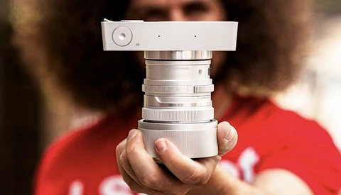 Hands holding a vintage rangefinder camera lens assembly with chrome barrel and focusing mechanism.