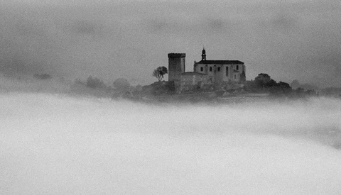 Medieval castle with tower and church spire emerging from dense fog and mist.