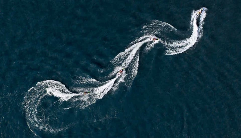 Aerial view of speedboat creating white wake patterns in dark blue ocean water.