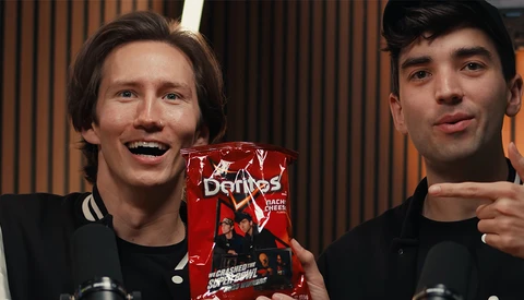Two men in black clothing holding a red box product, smiling at camera in studio setting.