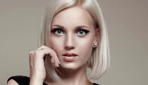 Portrait of a woman with platinum blonde bob and dramatic eye makeup against neutral background.