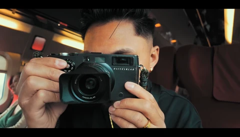 Photographer holding a teal rangefinder camera up to eye level, shot from inside a vehicle with warm interior lighting.