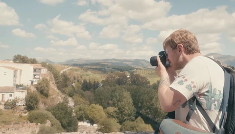 Photographer holding camera to face, composing a shot of rolling hills and forested landscape.