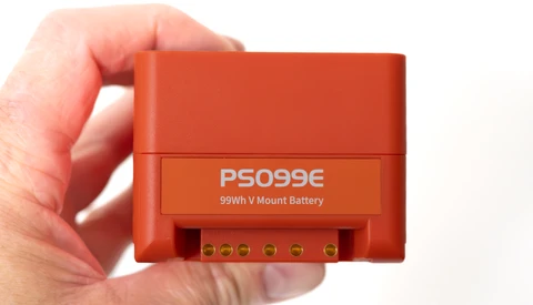 Red PS099E 99Wh V-mount battery held in hand, showing terminal connectors on front panel.