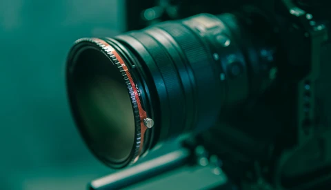 Close-up of a telephoto lens with red focus ring mounted on a camera body against a teal-colored background.