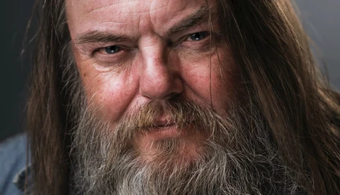 Bearded man with long hair and intense expression in close-up portrait.