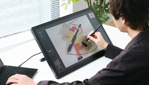 Designer using a stylus on a digital drawing tablet displaying abstract graphic artwork in progress.