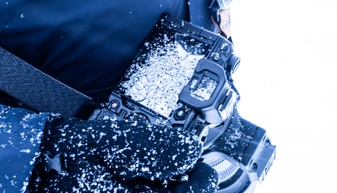 Digital watch covered in snow and ice against a blue winter background.