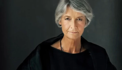 Mature woman with gray hair in black shirt against dark background.