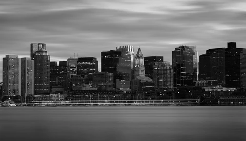 Monochrome cityscape with illuminated skyscrapers reflected in still water at dusk.