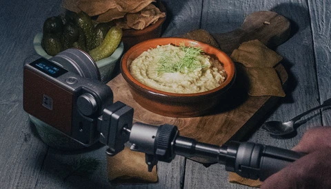 Film camera mounted on tripod with hummus and food styling setup on wooden surface.