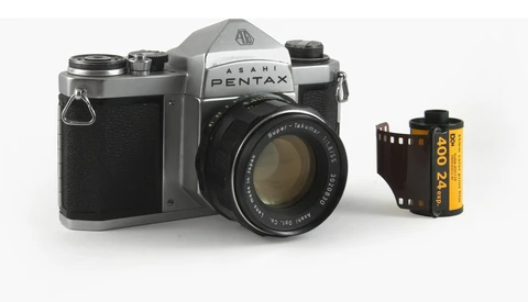 Asahi Pentax 35mm film camera with standard lens, shown alongside a roll of yellow Kodak film.