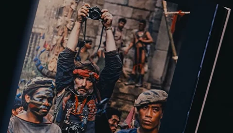 Photographer holding camera overhead while street performers pose below in urban setting.