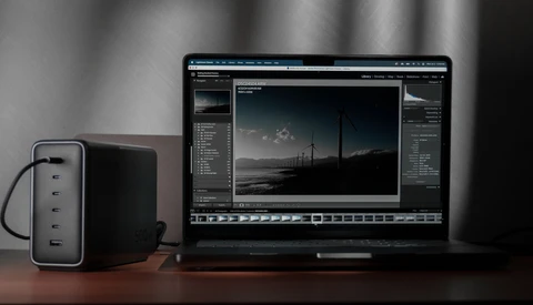 Photography editing workstation with laptop displaying RAW image in post-processing software and external power adapter.