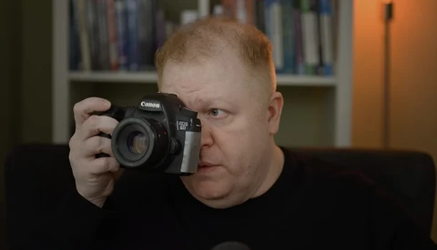 Photographer holding a Canon DSLR camera up to his face while looking intently through the viewfinder.