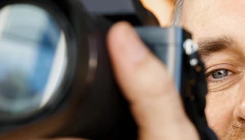 Male photographer looking through a telephoto lens with shallow depth of field focus on his eye.