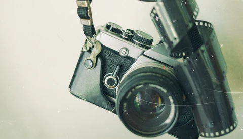 Vintage SLR camera with attached light meter and film strip arranged on neutral background.