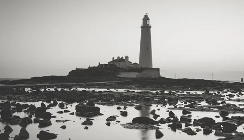 Lighthouse on rocky tidal flats under overcast sky in black and white.