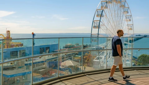 Runner jogging on a seaside boardwalk with a Ferris wheel and amusement park visible in the background.