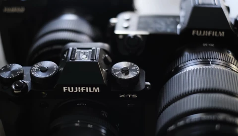 Fujifilm X-T5 camera with attached lens and additional camera gear in background.