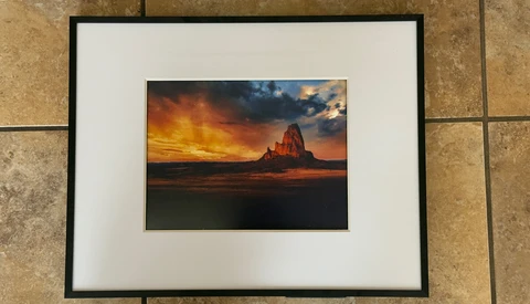 Framed photograph of a dramatic sunset over a desert rock formation with golden and orange sky.
