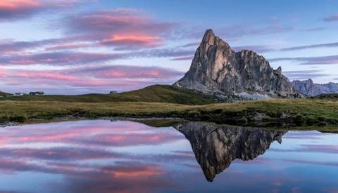 Rocky mountain peak reflected in still water at sunset with pink and purple sky.