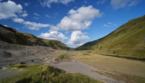 Alpine valley with braided river, grassy slopes, and dramatic sky with white clouds.