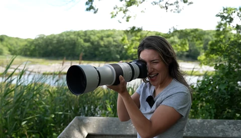 Photographer with telephoto lens overlooking a wetland landscape with reeds and trees.