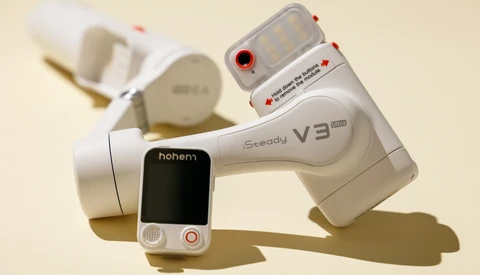 Three white handheld video stabilizers and a smartphone mounted on a neutral beige surface with soft shadows.