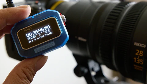 A blue GPS watch displaying navigation data held in front of a camera with telephoto lens.