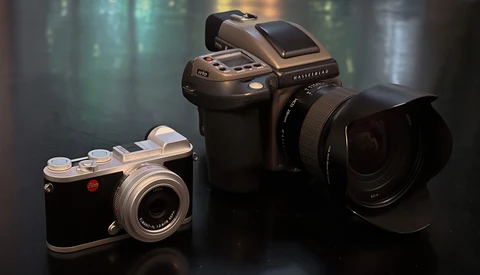 Three medium format cameras arranged on a dark surface with soft studio lighting and blurred background.
