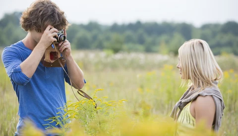 Young photographer with camera photographing a woman in a wildflower field.