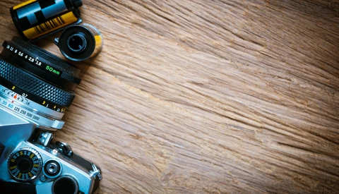 Vintage camera with interchangeable lenses and film rolls arranged on wooden surface.