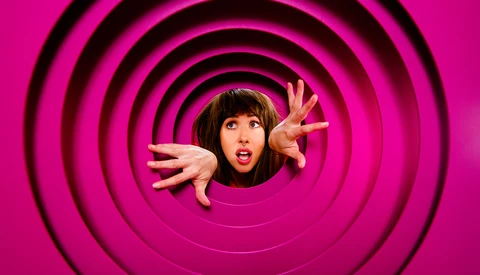 Person with surprised expression emerging from center of concentric black circles on magenta background.