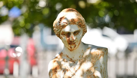 Weathered golden bust sculpture with shallow depth of field and blurred background.
