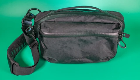 Black shoulder bag with multiple zippered compartments and an adjustable strap against a teal background.