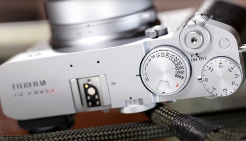 Top-down view of a white mirrorless camera with manual control dials and lens visible on textured fabric surface.