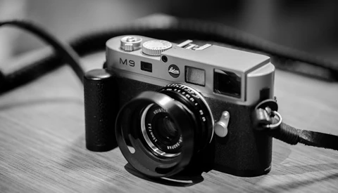 Leica M9 rangefinder camera with black leather strap on wooden surface.