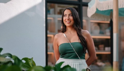Woman in green halter top and white skirt smiling outdoors in natural sunlight.