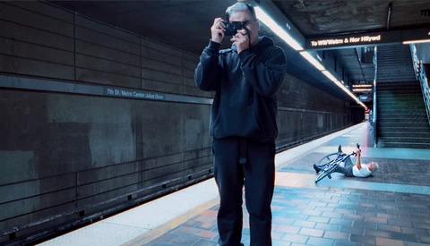 Man in dark suit and sunglasses holding camera at subway station platform.