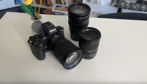 Nikon camera body with three interchangeable lenses arranged on a white surface.