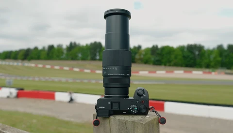 Sony mirrorless camera with telephoto lens mounted on wooden post overlooking racing circuit.