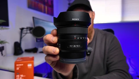 Sony lens with f/1.8/16 aperture being held up for display in a studio setting.