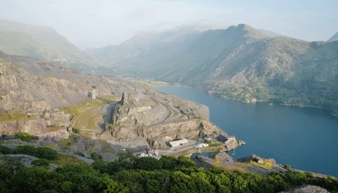 Medieval fortress on a rocky peninsula overlooking a deep blue alpine lake surrounded by mountains.