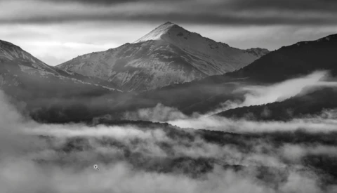 Mountain peak rising above a thick blanket of clouds in a misty valley at dawn.