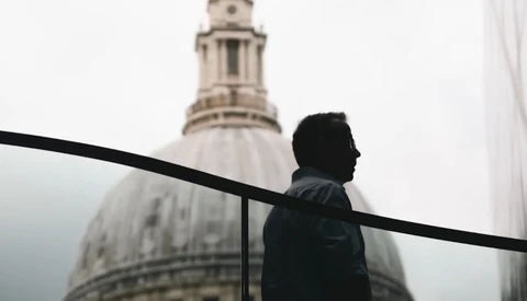 Man in dark jacket silhouetted against a domed building in fog.