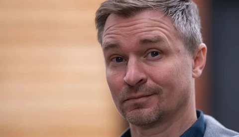 Man with gray hair and facial hair looking at camera with a skeptical, slightly puzzled expression.