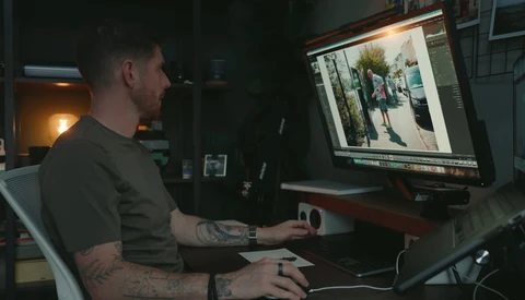Photographer editing images on a desktop computer in a dark studio workspace.