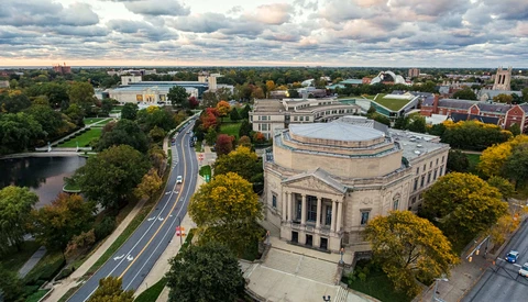 Aerial view of a domed classical building surrounded by trees and urban landscape with river.